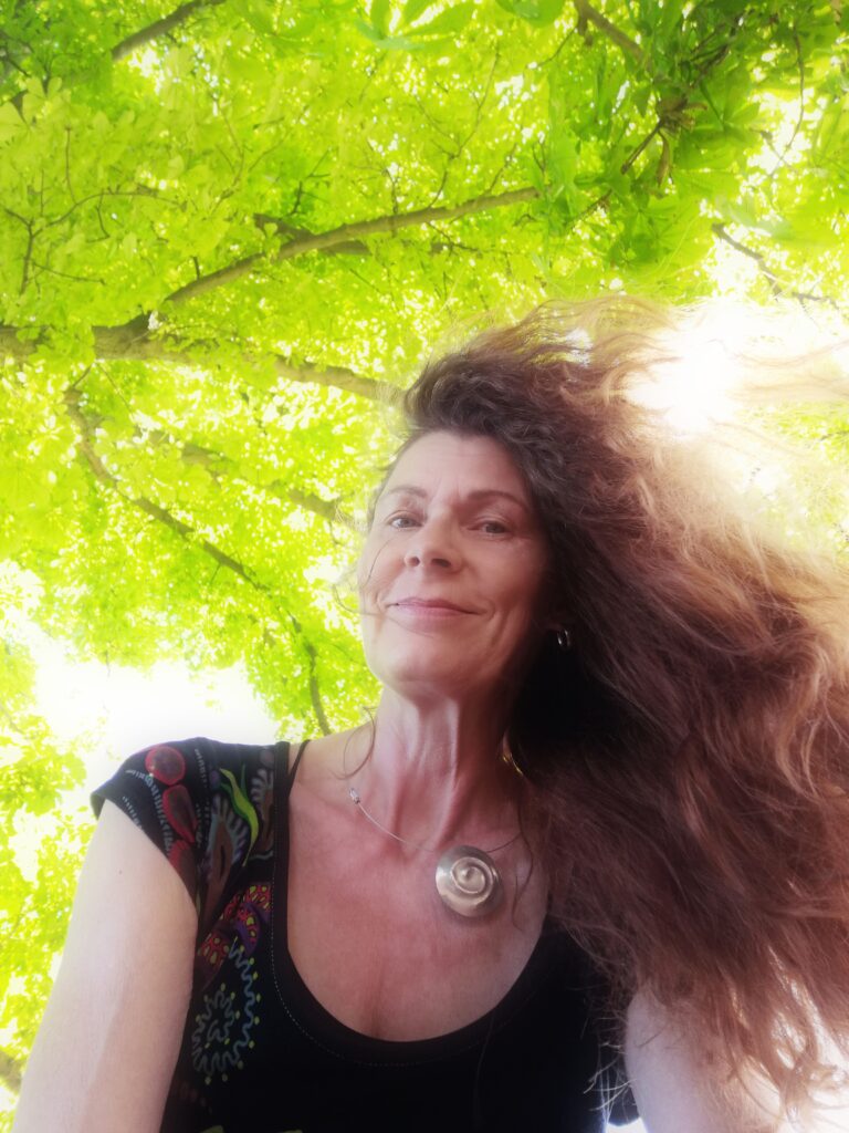 Frau mit langen Haaren ober ihr grüne Baumkronen