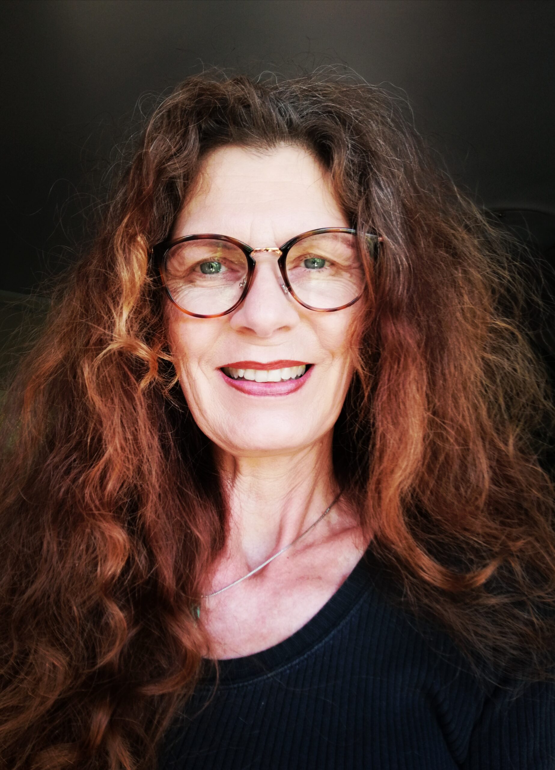 Portrait einer Frau, sie trägt Brillen und hat rötliche Haar und lächelt