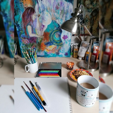 Im Atelier - Stifte und Papier liegen am Tisch, ein Gemälde davor und eine Tasse Kaffe steht rechts danaben